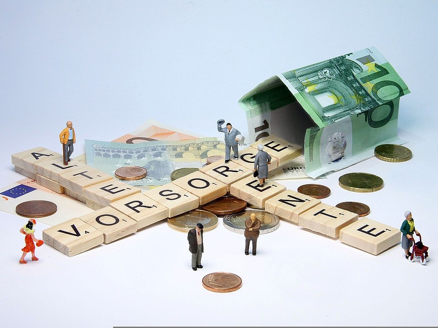 Foto: Scrabble-Buchstaben formen die Worte Alter, Vorsorge und Rente. Mehrere Geldscheine, Münzen und kleine Figuren sind zu sehen.