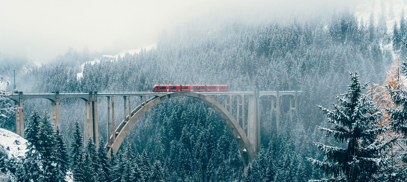 Roter Zug fährt durch Winterlandschaft.