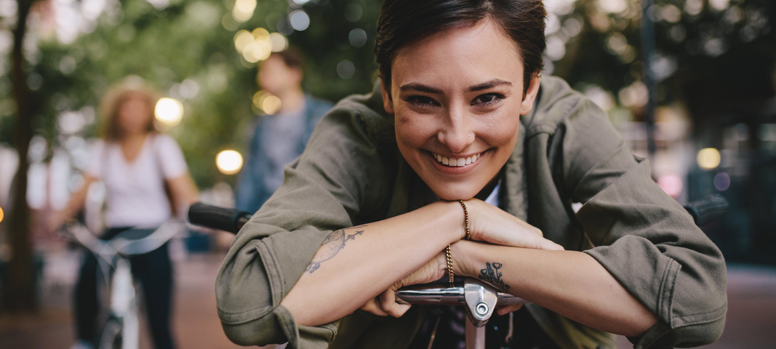 Porträt einer glücklichen Frau, Sie lehnt auf ihrem Fahrrad mit Freunden im Hintergrund. Alle genießen einen Tag in der Stadt mit ihrem Fahrrad.